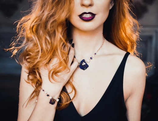 close-up portrait of young beautiful red-haired girl in the image of a Gothic witch on Halloween on a background of wax candles, fire, magic crystals and stones in the black dress conjures