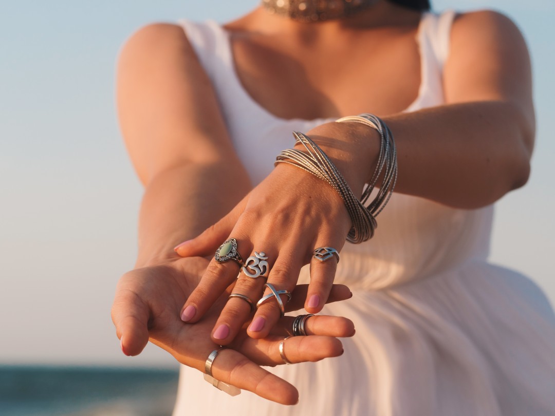 close up hands with boho gypsy silver accessories. Woman standing on the beach at summer near sea.