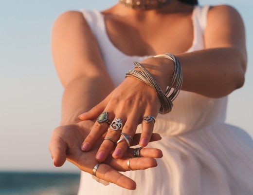 close up hands with boho gypsy silver accessories. Woman standing on the beach at summer near sea.