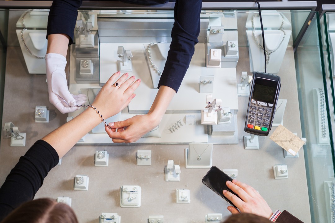 Young woman trying on golden bracelet, man going to pay with credit card