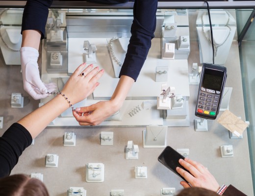 Young woman trying on golden bracelet, man going to pay with credit card